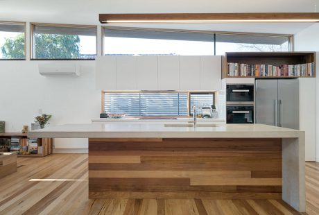 Sleek modern kitchen with wood-paneled island, built-in shelves, and large windows.