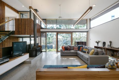 Sleek modern living room with large windows, wood beams, and an angular fireplace.