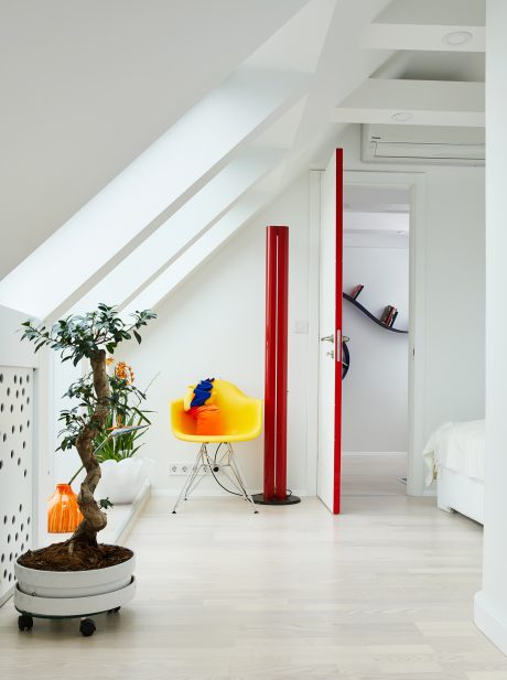 Modern, minimalist space with sleek white walls, angular red accents, and potted plant.