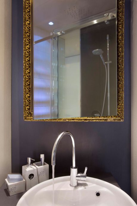 A stylish bathroom with a gilded mirror frame, modern faucet, and minimalist accessories.