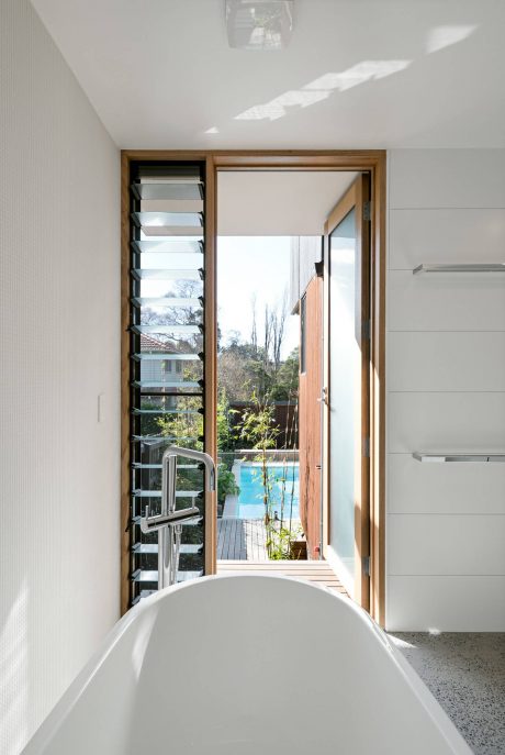 A modern, minimalist bathroom with a freestanding tub and a view of the lush outdoor garden.