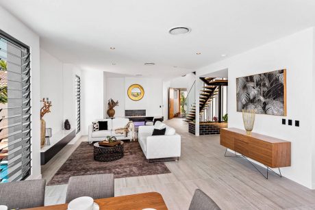 Sleek, modern living space with wooden accents, palm leaf artwork, and a floating staircase.