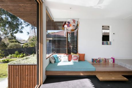 Cozy reading nook with a built-in daybed, colorful pendant lamp, and wood-paneled wall.