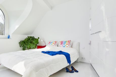 Bright, minimalist bedroom with slanted ceiling, large window, and colorful accents.