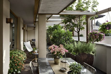 Covered patio with lush greenery, glass walls, and a cozy seating area.