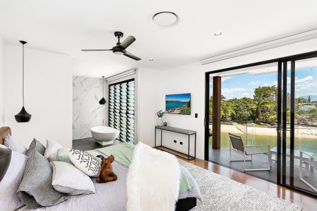 Luxurious bedroom with modern decor, marble wall, and panoramic views of lush outdoor landscape.