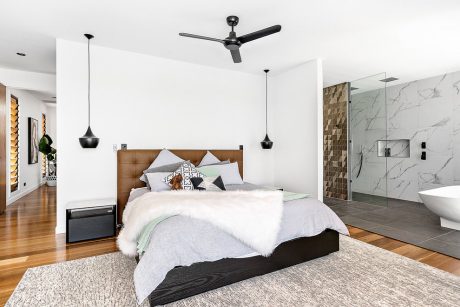 Spacious modern bedroom with wooden headboard, pendant lights, and marble shower.