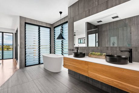 Sleek, modern bathroom with wood and gray tones, freestanding tub, and window-mounted shutters.
