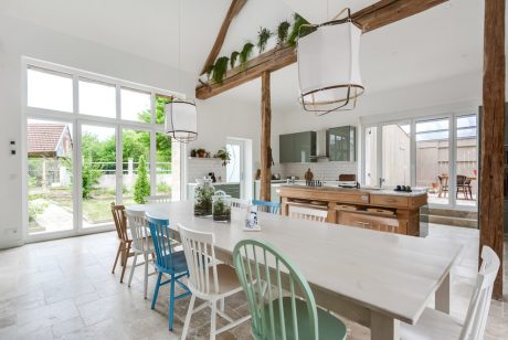 Bright, modern kitchen with rustic wooden beams, contrasting chairs, and large windows.