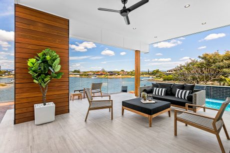 Modern patio with wooden walls, pool, and scenic lakeside view. Stylish furniture.