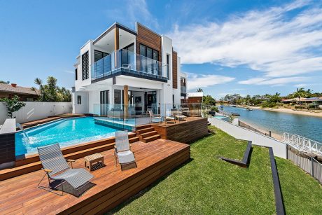 Striking modern home with sleek wooden exterior, expansive terrace, and pool overlooking water.