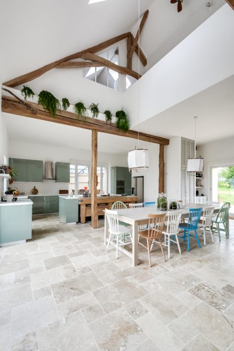 A spacious open-concept kitchen and dining area with exposed wooden beams and greenery.