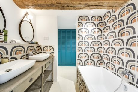 A modern bathroom with a patterned accent wall, wooden ceiling beams, and a teal closet.