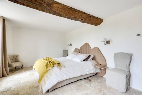 Rustic bedroom with wooden beams, neutral tones, and a distinctive headboard design.