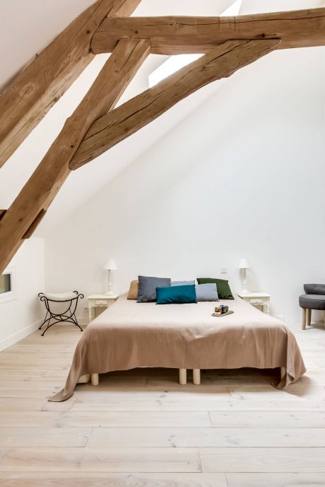 Rustic wooden beams accent the modern white bedroom with colorful pillows on the bed.