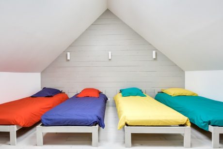 A cozy attic space with four twin beds dressed in vibrant bedding on simple wooden frames.