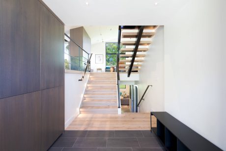 Elegant staircase with wooden steps and modern glass railing leads to upper level.