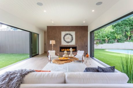A modern, open-concept living space with sleek fireplace, plush furnishings, and expansive windows overlooking a lush outdoor area.