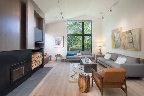 A modern living room with large windows, gray sofas, and colorful abstract artworks.