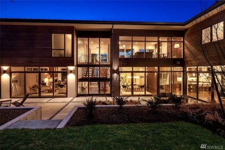 Sleek, contemporary exterior with large windows, illuminated at night, surrounded by landscaping.