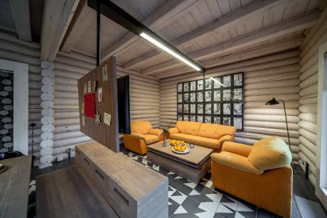 Cozy log cabin interior with rustic wooden ceiling, warm yellow furniture, and geometric tiled floor.