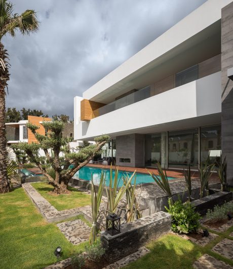 Modern architectural design with sleek lines, glass panels, and lush landscaping surrounding a swimming pool.