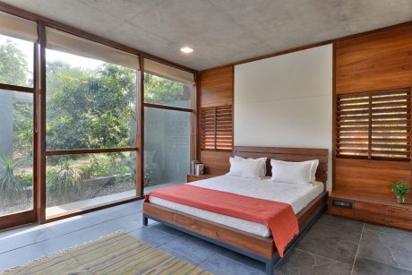 Spacious wooden bedroom with large windows overlooking lush greenery, minimal decor.
