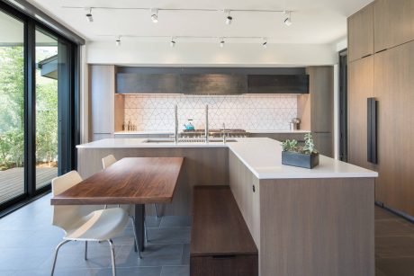 Sleek, modern kitchen with wooden accents, island counter, and large windows overlooking nature.