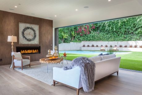 Spacious modern living room with fireplace, lush outdoor view, and plush furnishings.