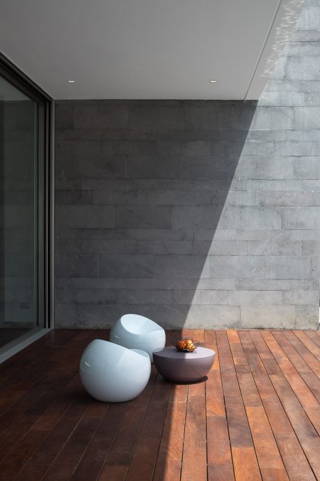 Minimalist concrete walls, wooden deck, and modern seating create a serene ambiance.