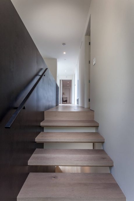Sleek, modern hallway with wooden stairs and a dark accent wall leading to a room.