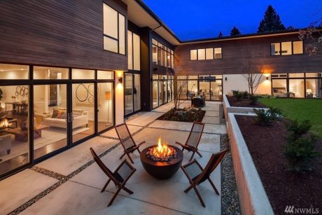 A modern, expansive home with a cozy fire pit and seating area surrounded by lush landscaping.