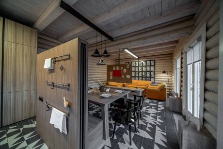 A cozy log cabin interior with wooden ceiling beams, wall panels, and patterned tile floor.