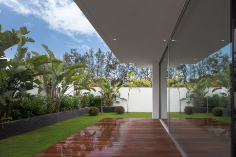Modern glass structure with lush tropical landscaping and wooden deck.