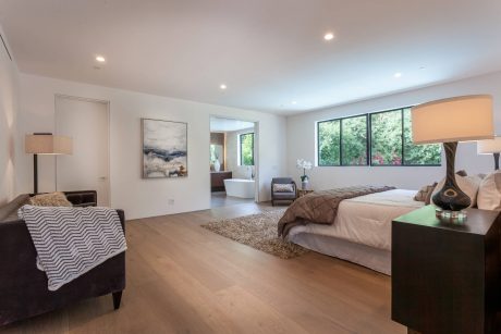 Spacious, modern bedroom with large windows, wood floors, and sophisticated decor.