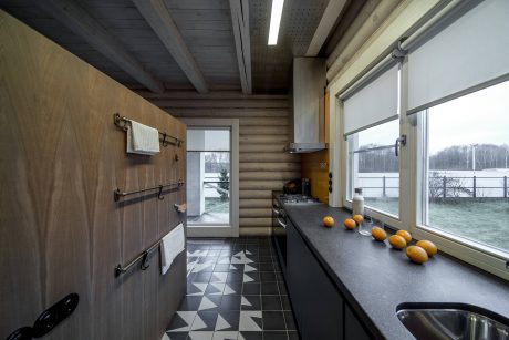 A rustic, modern kitchen interior with wooden beams, tile flooring, and large windows offering scenic views.