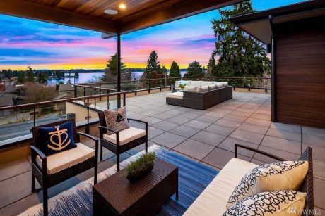 A spacious, modern deck with a panoramic view of a sunset over a lake, surrounded by lush greenery.