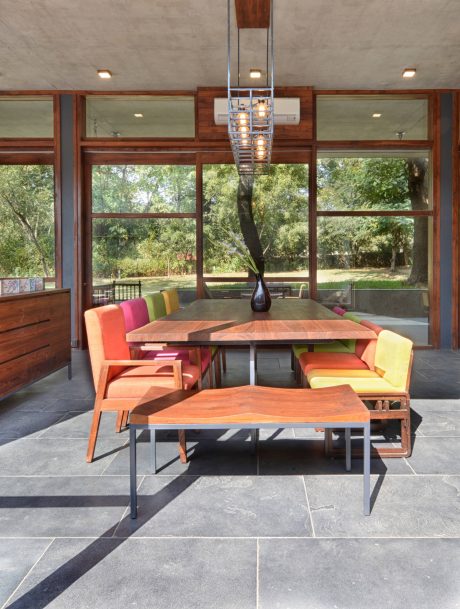 Bright, modern dining space with wooden furniture, sleek lighting, and floor-to-ceiling windows overlooking nature.