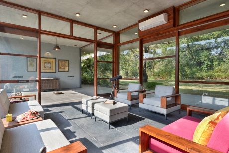 Expansive glass-encased living space with sleek wooden furniture and lush outdoor views.