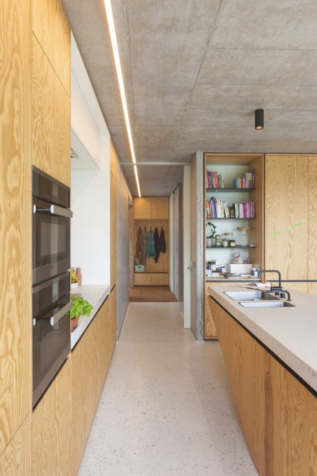 A modern, minimalistic kitchen and hallway with wood paneling and open shelving.