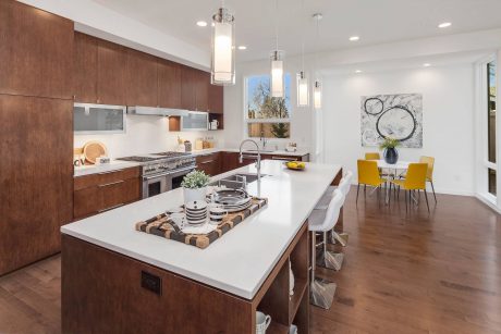 Sleek modern kitchen with warm wooden cabinetry, white countertops, and stylish pendant lights.