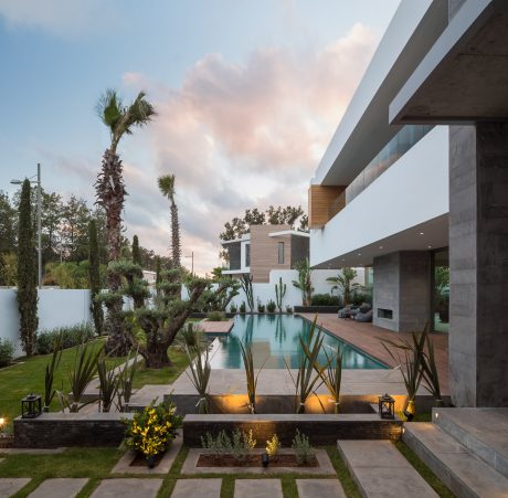 A modern, minimalist home with a sleek pool, lush landscaping, and warm lighting.