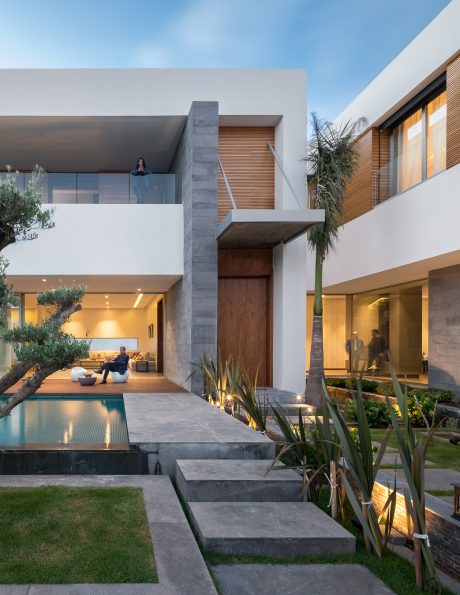 A modern, minimalist house with concrete and wood accents, a pool, and lush landscaping.