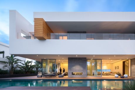 A modern, minimalist home with sleek lines, glass walls, and a shimmering pool reflecting the sky.