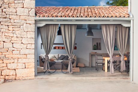Cozy outdoor living space with stone walls, tiled roof, and curtained entryway.