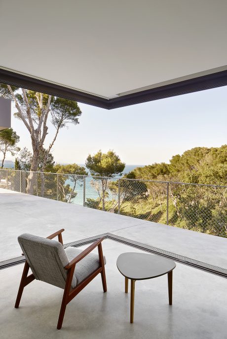 Modern outdoor patio with wooden furniture, glass walls, and scenic ocean view.