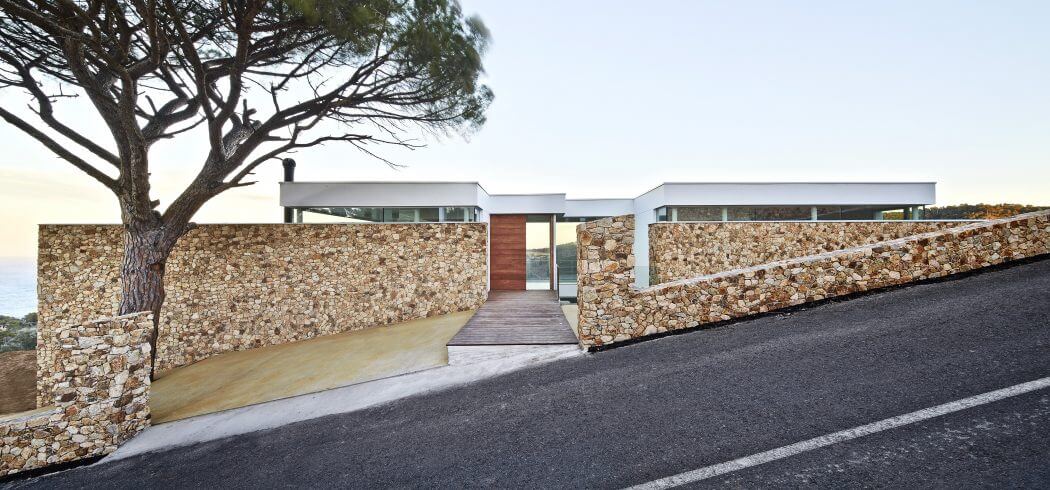 Modernist stone and concrete villa with a curved stone wall and walkway leading to the entrance.