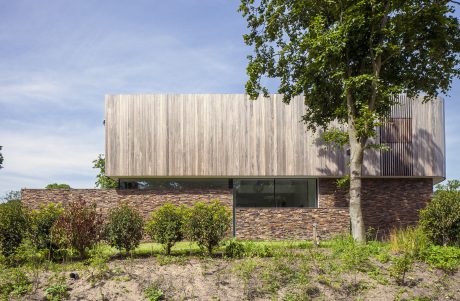 A modern, wooden-clad structure with a stone-clad base, nestled among lush greenery.