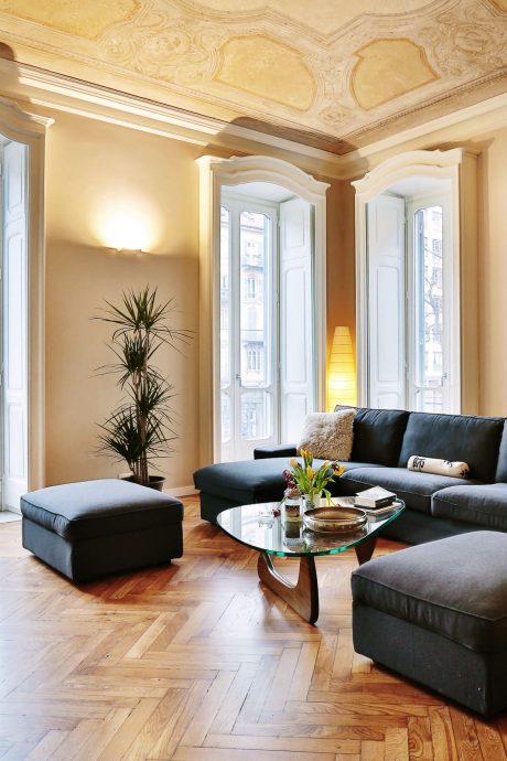 Elegant living room with ornate ceiling, arched windows, black leather furniture, and glass coffee table.