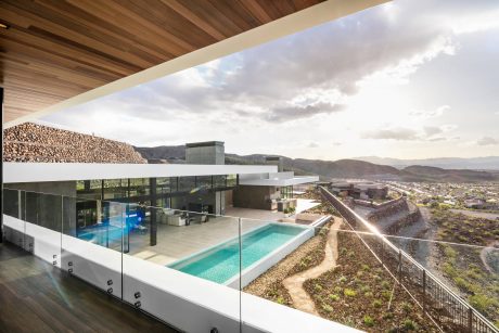 A modern, glass-walled home with a pool overlooking a mountainous landscape.